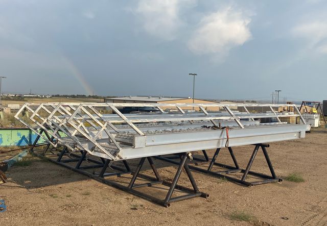 Row of finished aluminum stairways with handrails resting on black steel stands in the yard, a rainbow in the cloudy sky behind