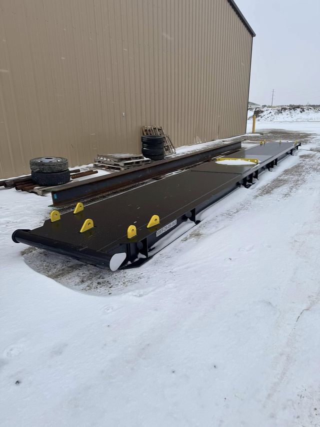 Black fabricated steel skid with yellow lifting lugs and a diamond-plate deck, in the snow outside the shop