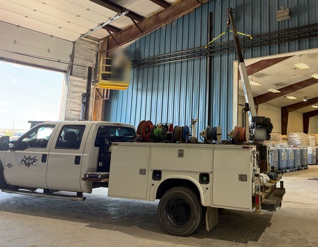 Side view of HWF&rsquo;s white Ford F-550 mobile welding rig: service body, crane and hose reels, HWF logo on the door, parked in a shop