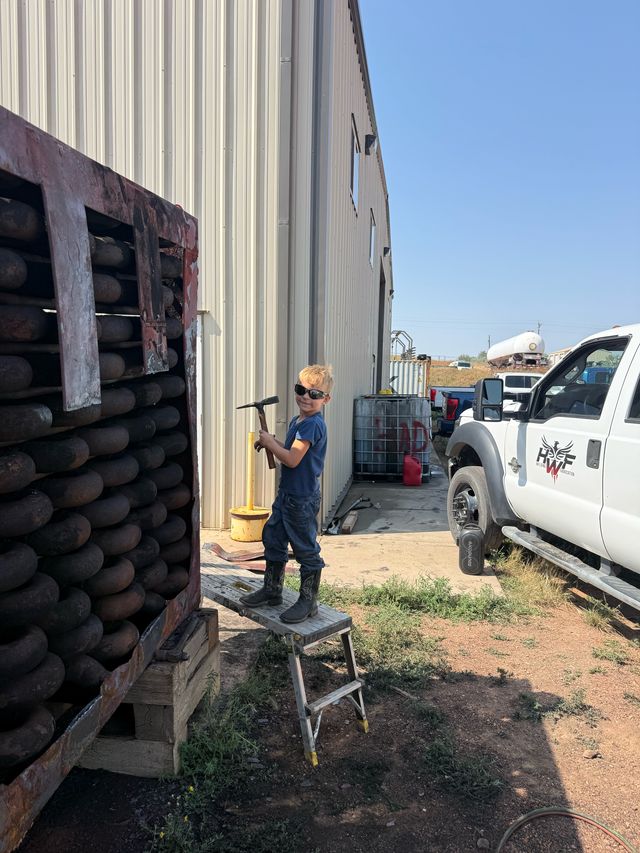 A young boy in sunglasses holding a hammer, standing on a step stool beside the HWF truck