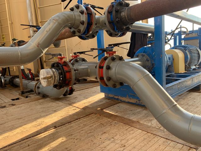 Low-angle view of gray pipe spools and butterfly valves tied into a pump and electric motor on a blue skid