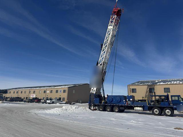 Blue truck-mounted rig with its derrick raised under a clear winter sky
