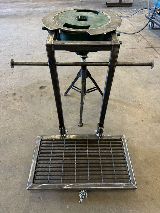 Steel rod stand with a green top plate, side handles and a hinged grated foot platform, on the shop floor