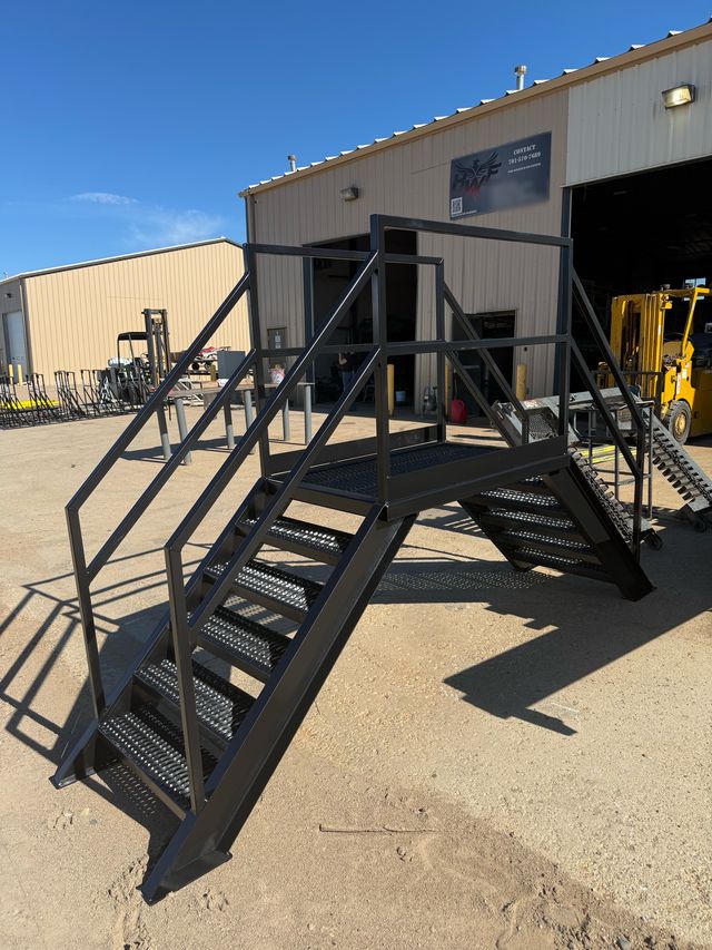Black steel crossover with grated stairs up both sides and a top platform, outside the HWF shop with the HWF sign on the wall