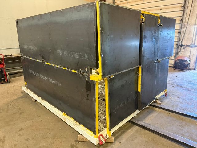 Large black steel wind wall enclosure with yellow trim and a white skid base, in the HWF shop
