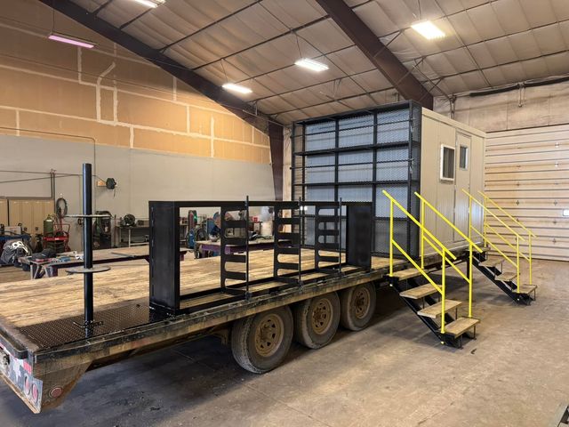 Trailer-mounted skid building with yellow stairs and handrails, inside the shop